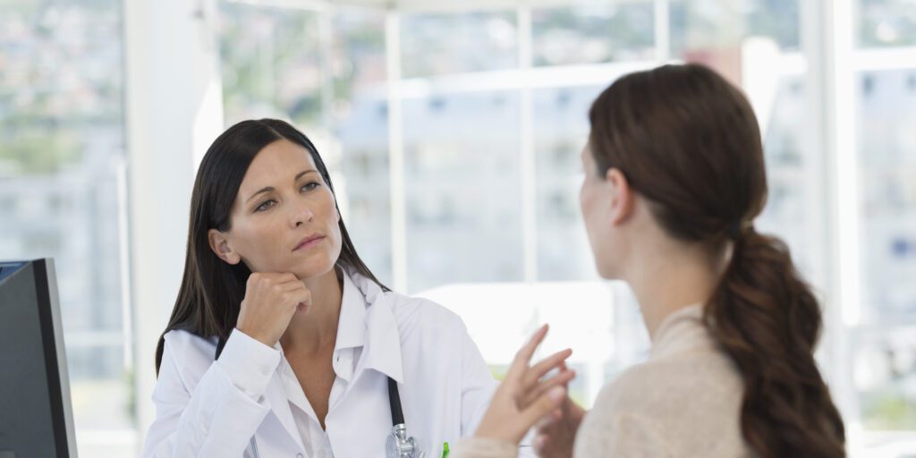 Doctor with a stethoscope thoughtfully listening to a woman explaining her symptoms during an appointment.