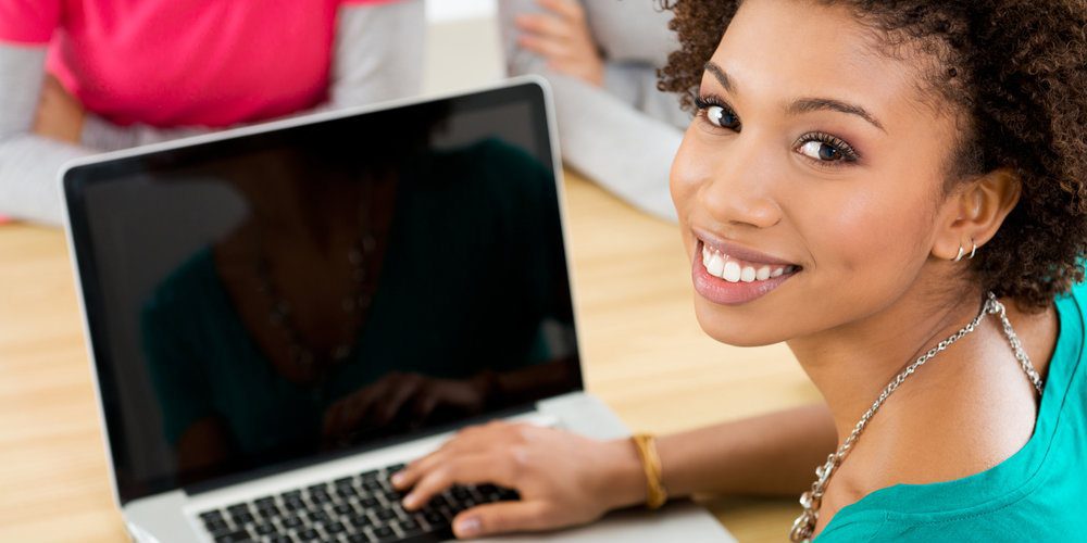 Happy professional sitting at desk with laptop computer, looking at camera.