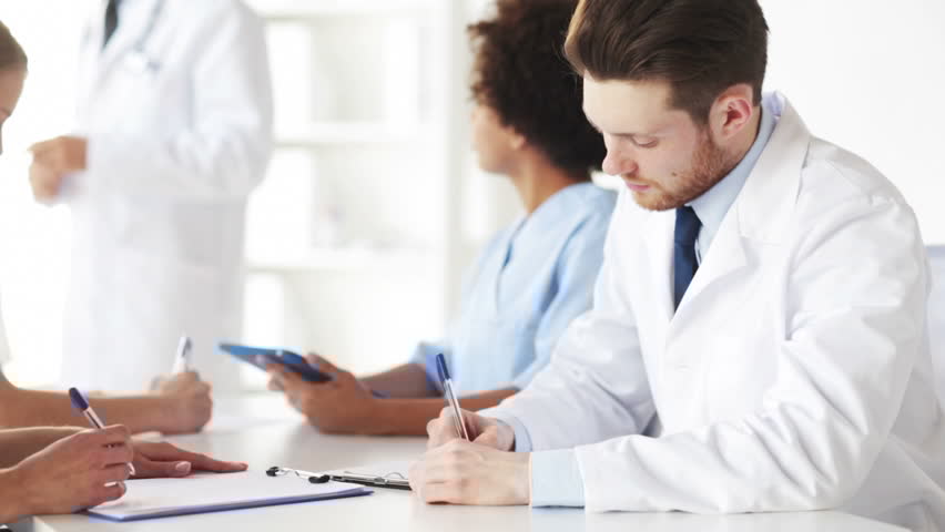 Medical professionals taking notes during a healthcare team meeting in a bright clinic.
