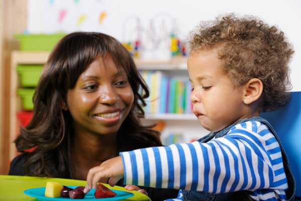 Caregiver interacting with a toddler who is selecting fruit from a colourful plate.
