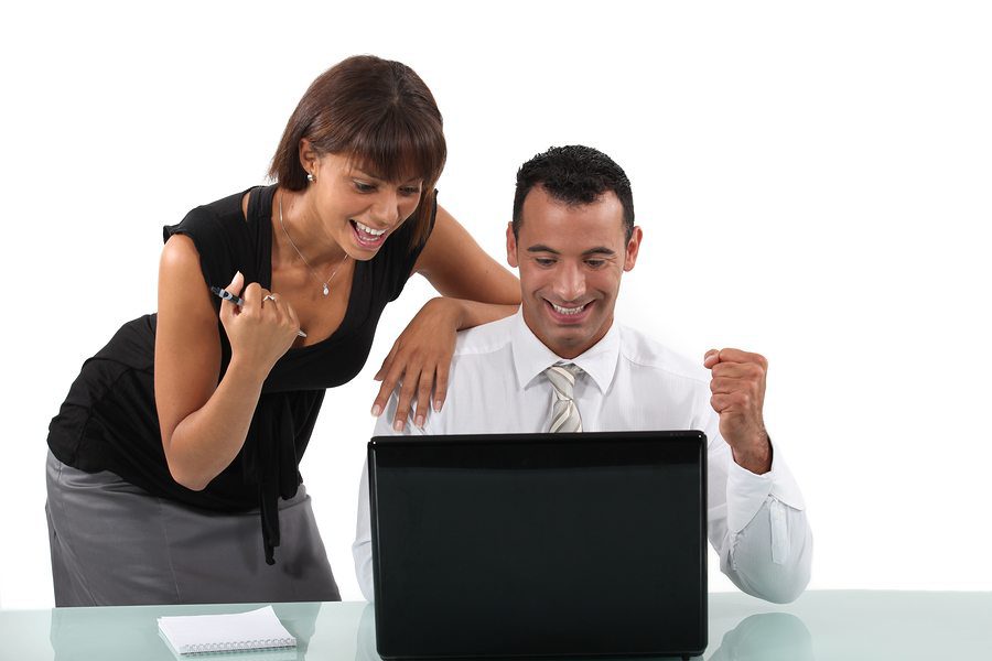 Smiling man and woman at a desk reacting happily to news on a laptop.