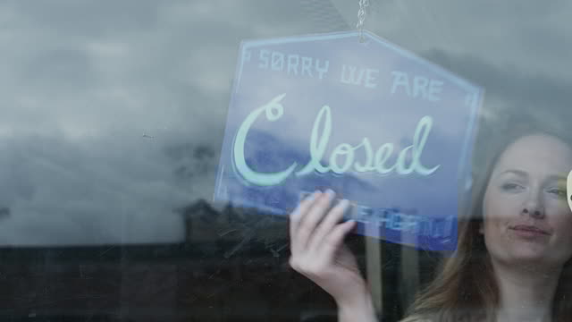 Woman flipping a sign on a glass door to show the business is closed.