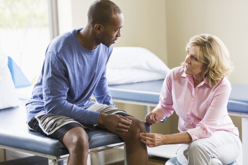 Physiotherapist examining a male patient’s knee during a consultation in a clinic.