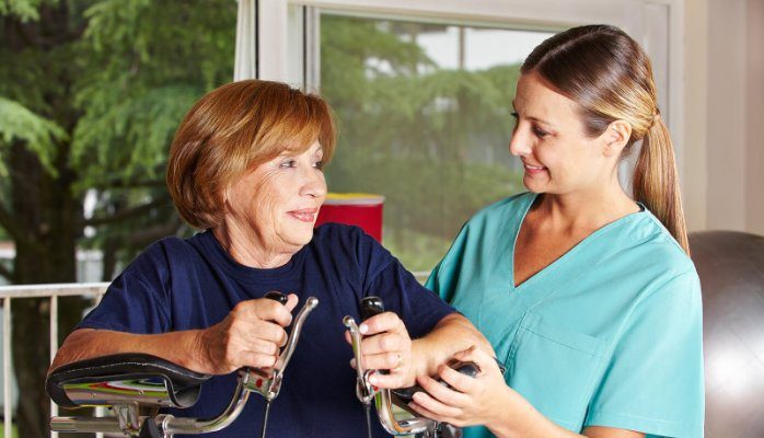 Physical therapist helping elderly woman with exercise equipment during rehabilitation.
