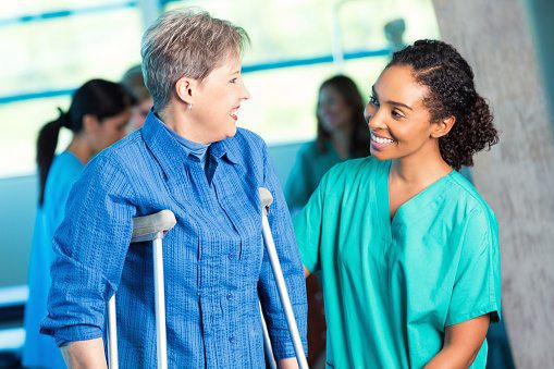 Smiling healthcare worker assisting a patient using crutches during rehabilitation.
