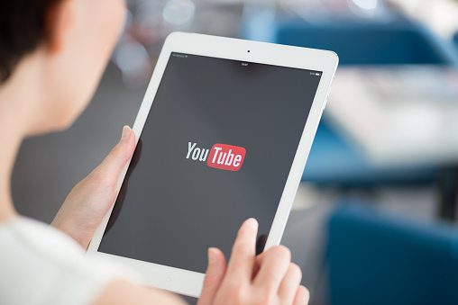 Person holding a tablet displaying the YouTube logo on the screen.
