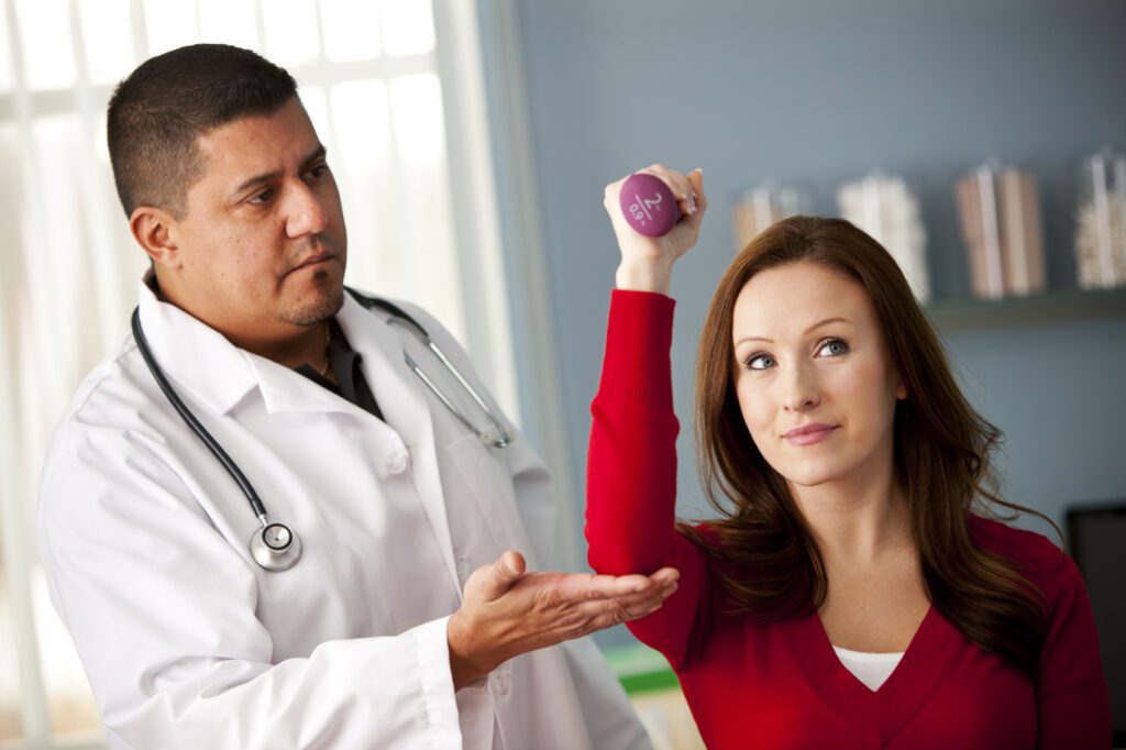 Doctor supervising a woman lifting a small dumbbell during a physical therapy session.