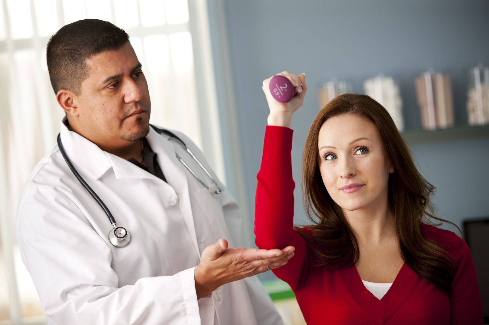 Doctor supervising a woman lifting a small dumbbell during a physical therapy session.