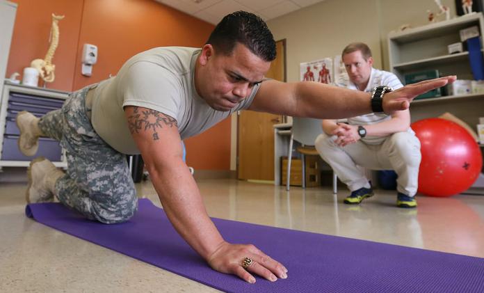 Physical therapist guiding a patient through a balance and strength exercise on a yoga mat.