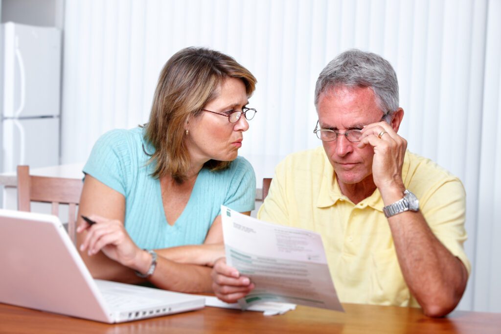 Man and woman looking concerned while reading paperwork beside a computer.