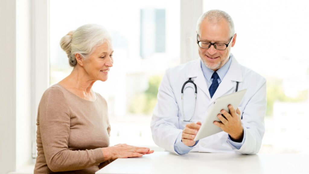 Smiling doctor showing information on a tablet to an older female patient during a consultation.