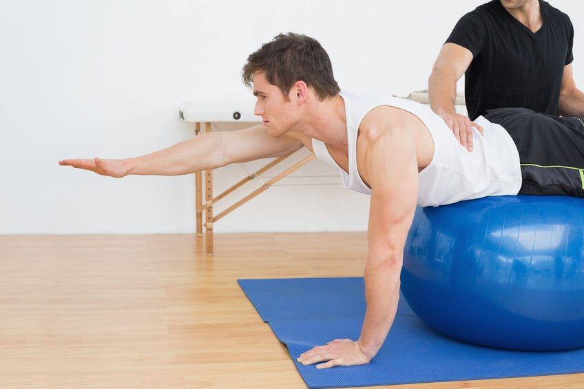 Physical therapist guiding patient through core stability exercise on a fitness ball.