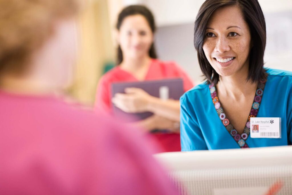 Healthcare professional greeting a patient while another nurse stands in the background with a clipboard.