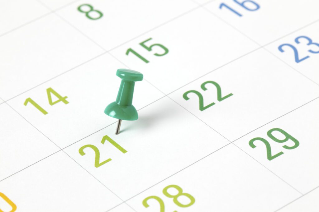 Green thumbtack pinned to a date on a printed calendar representing an appointment or reminder.