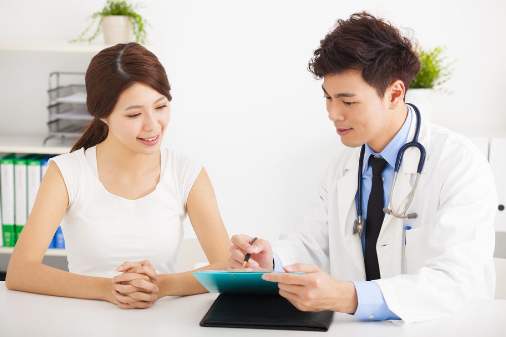 Healthcare professional reviewing treatment notes with a young woman at a doctor’s office.