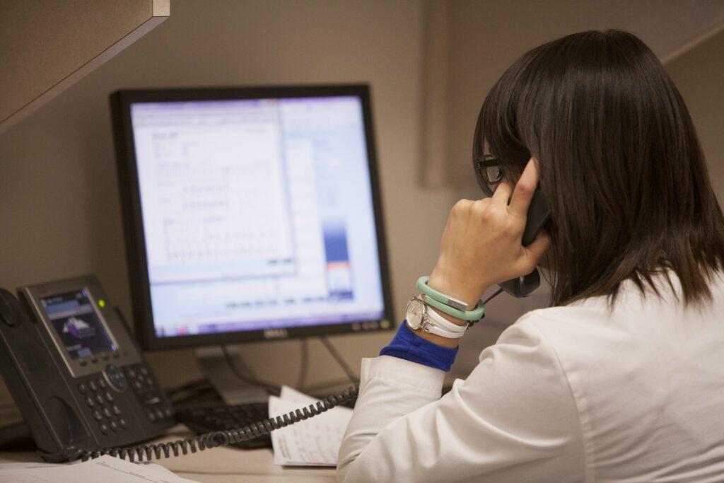Medical office staff member speaking on the phone while reviewing patient data on a computer screen.