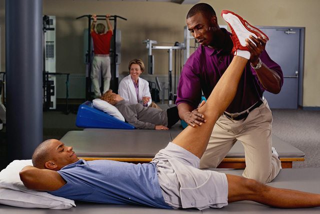 Physiotherapist using a handheld therapy device on a woman’s shoulder during a treatment session.
