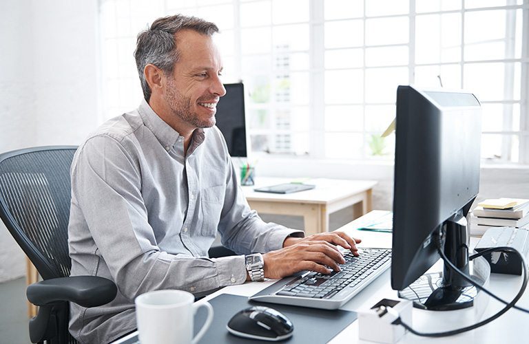 Middle-aged professional typing on desktop computer while seated in an ergonomic chair.