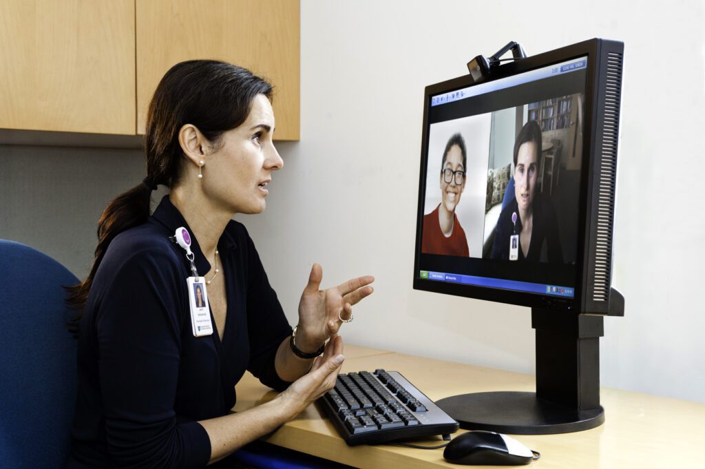 Medical practitioner engaged in an online appointment with patients displayed on a computer monitor.