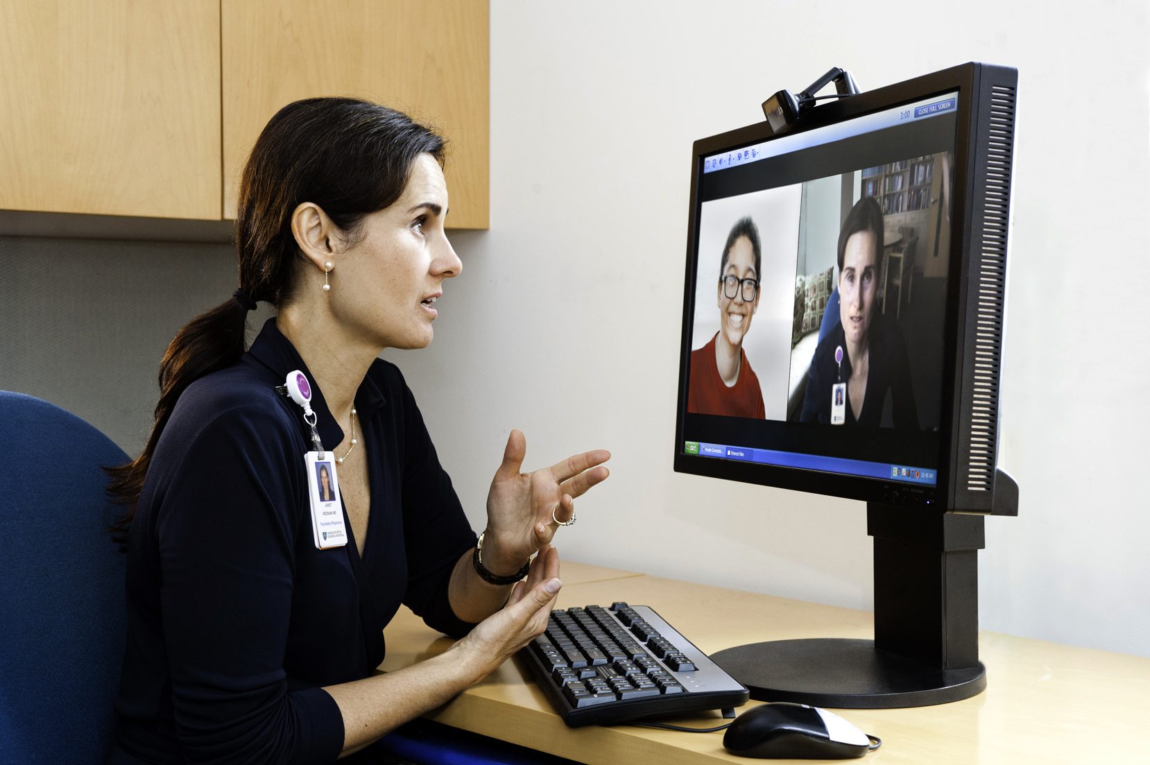 Medical practitioner engaged in an online appointment with patients displayed on a computer monitor.