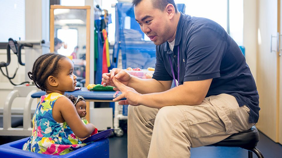 Speech therapist working with young child during therapy session using play-based techniques.
