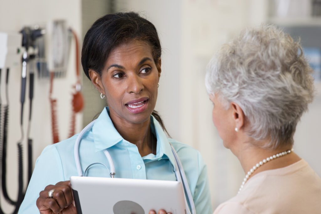 Healthcare professional discussing medical records on tablet with elderly woman.