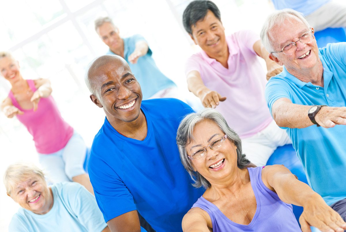 Diverse group of smiling seniors participating in a group physiotherapy session.