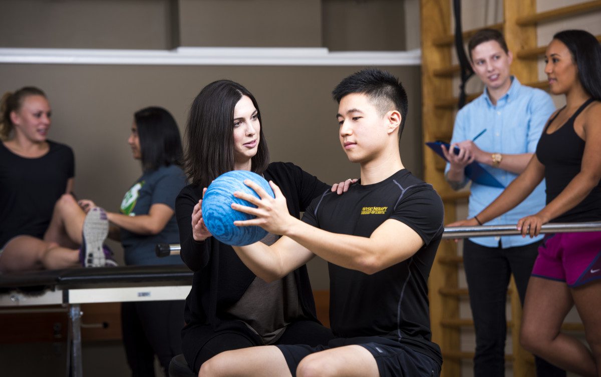 Physiotherapy students practising rehabilitation exercises with a medicine ball in a clinical training setting.