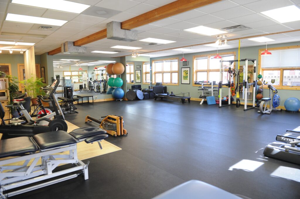 Spacious physiotherapy and rehabilitation clinic with exercise equipment, treatment tables and large windows.