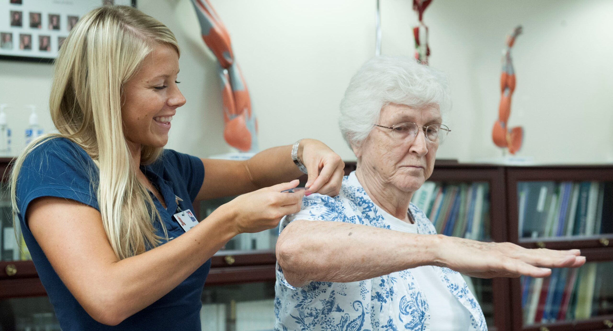 Physiotherapist assisting senior woman with shoulder mobility exercise during rehabilitation session.