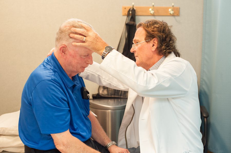 Doctor examining an older male patient’s head and neck during a medical assessment in a clinic.