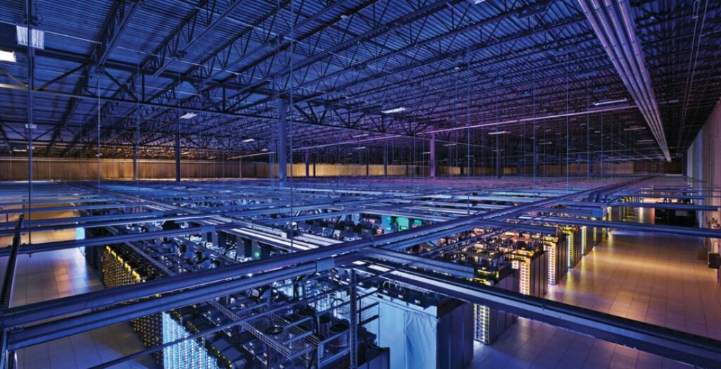 Modern data center with illuminated server racks and network cables under blue lighting.