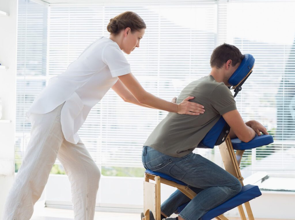 Manual therapy session with practitioner massaging patient’s back using massage chair.