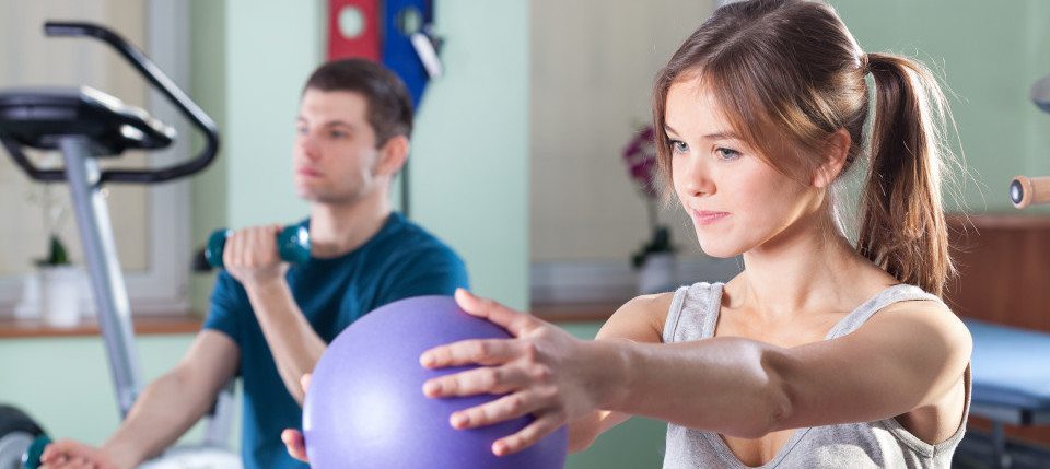 Patients performing physical therapy exercises with fitness equipment in rehabilitation clinic.