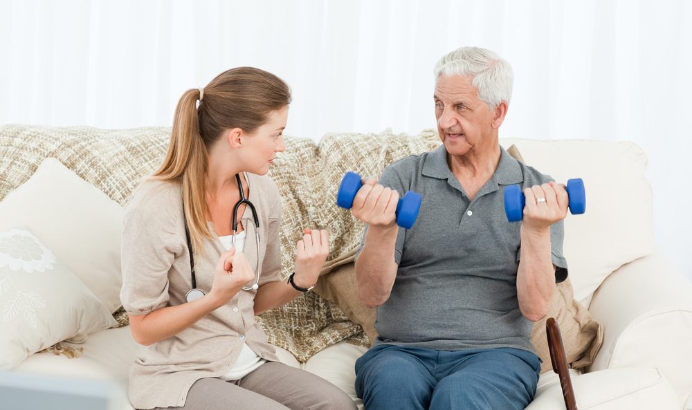 Physical therapist assisting elderly man with strength exercises using dumbbells at home.