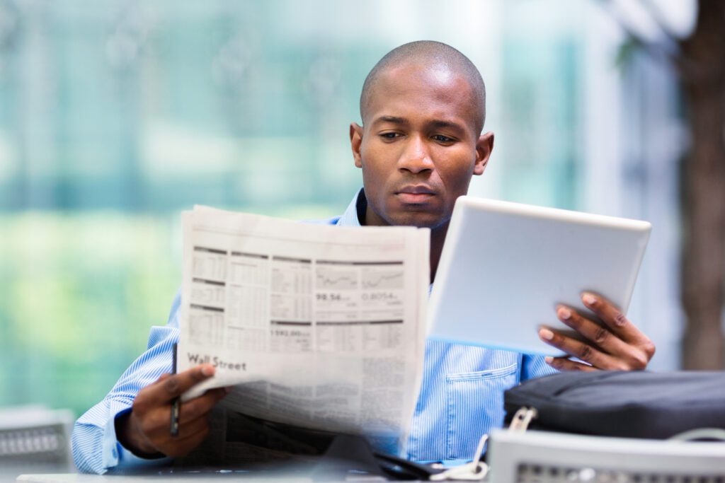 Businessman analyzing market updates on paper and digital device.