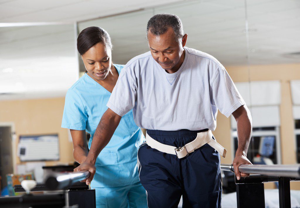 Rehab therapist helping a man walk using parallel bars for physical therapy.