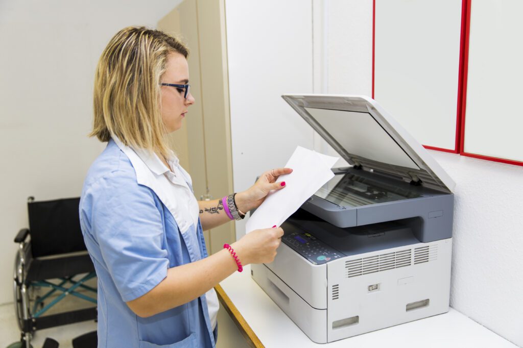 Healthcare worker sending patient paperwork through a fax machine in clinic.