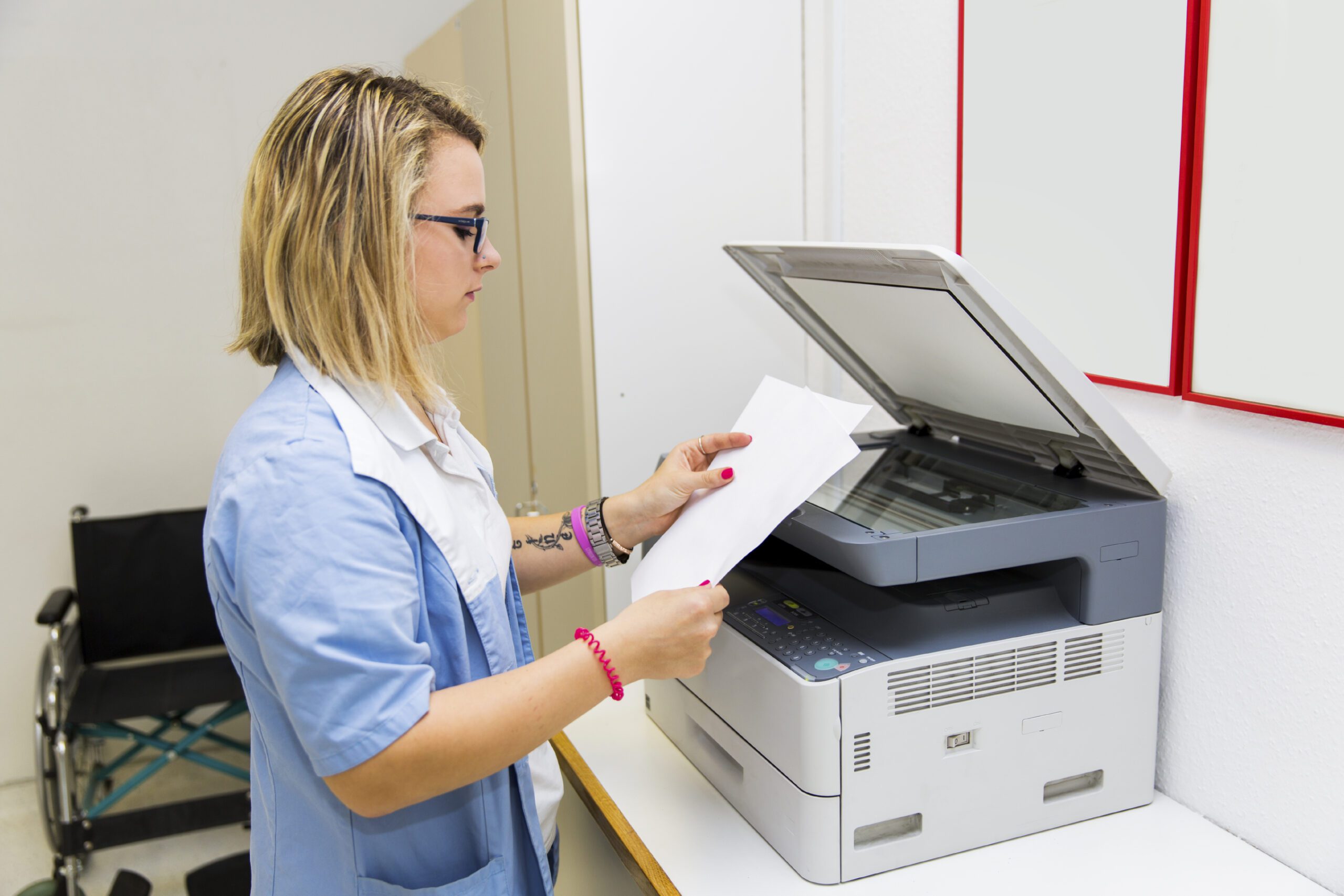 Healthcare worker sending patient paperwork through a fax machine in clinic.