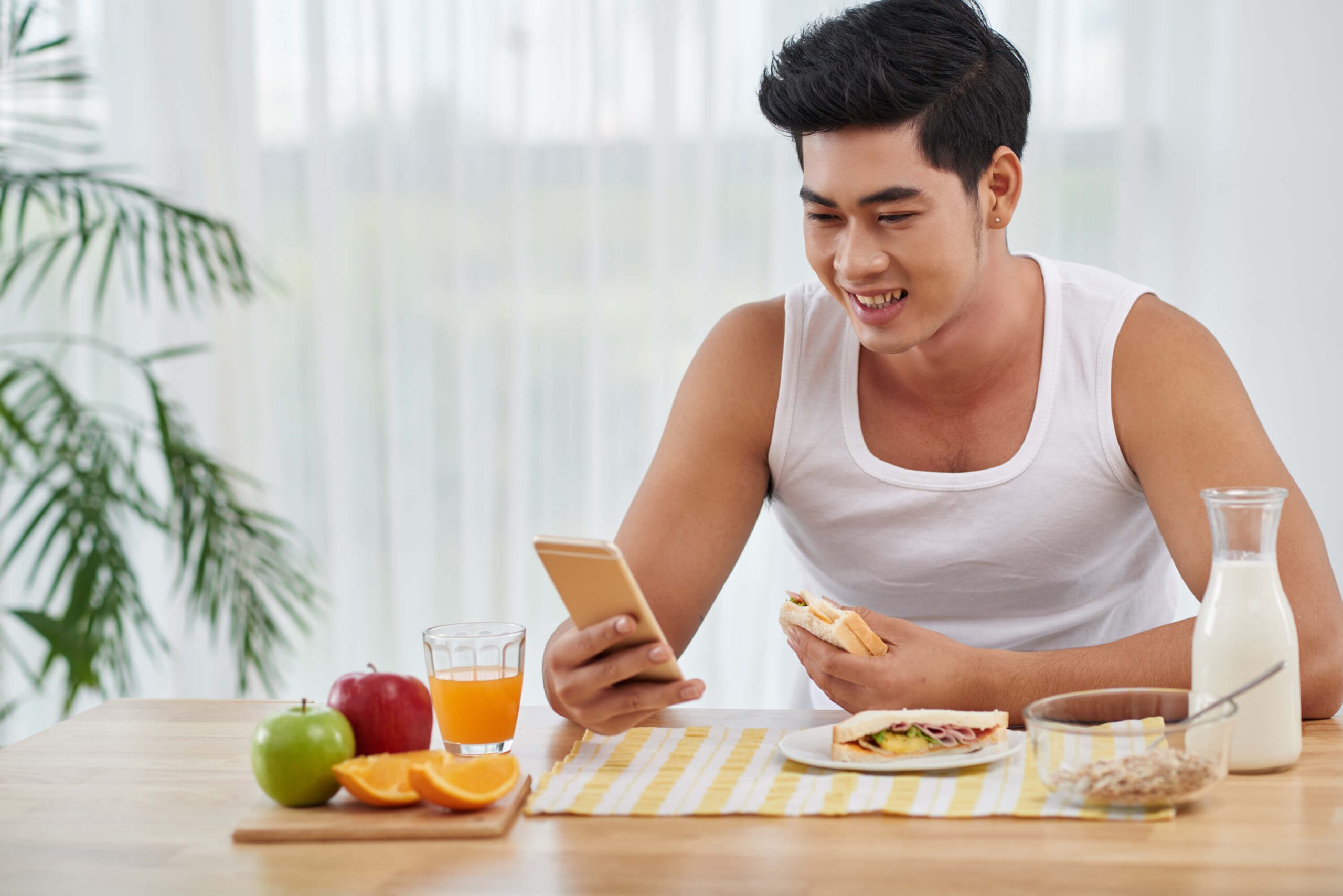 Young man checking automated text message while eating breakfast at home.