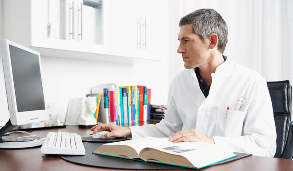 Physician reviewing medical records and documentation on desktop system.