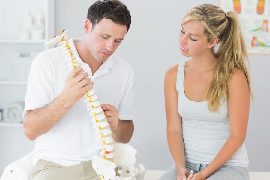 Healthcare professional discussing back structure with patient using spine model.