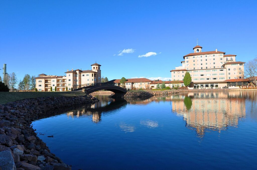 The Broadmoor Resort in Colorado Springs, venue for the PPS 2018 Conference, reflected in a calm lake under a clear blue sky.