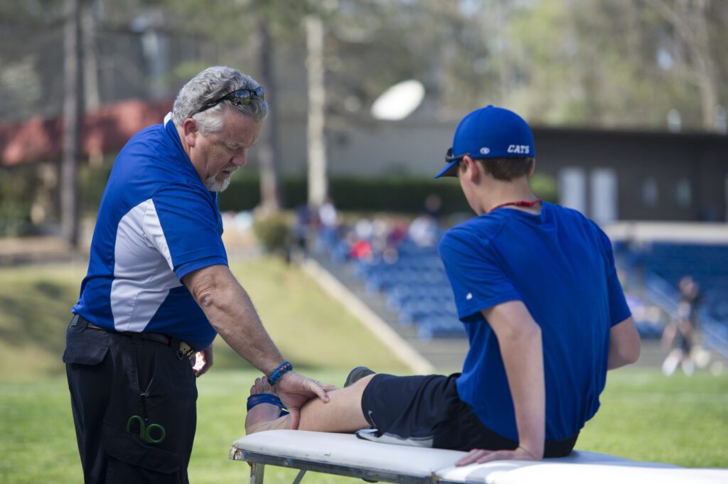 Sports therapist treating a young athlete’s leg injury on the sidelines during outdoor training.