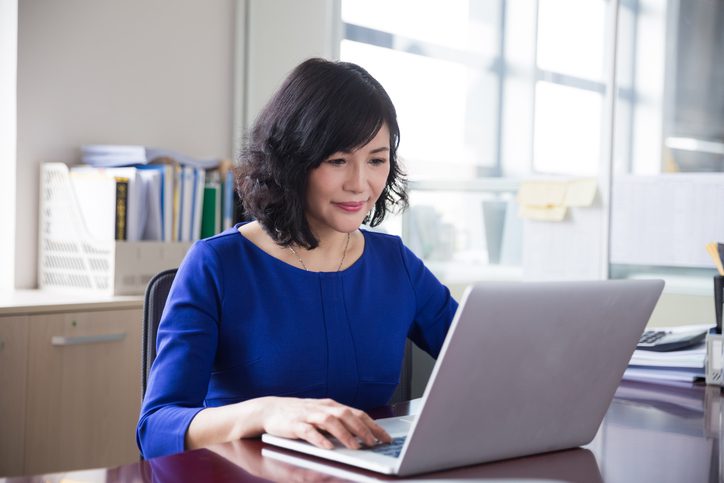Businesswoman typing on computer at her desk with documents and files in the background.