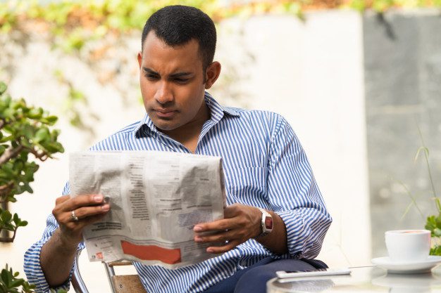 Man reading newspaper outdoors with coffee, representing healthcare business updates and industry news.