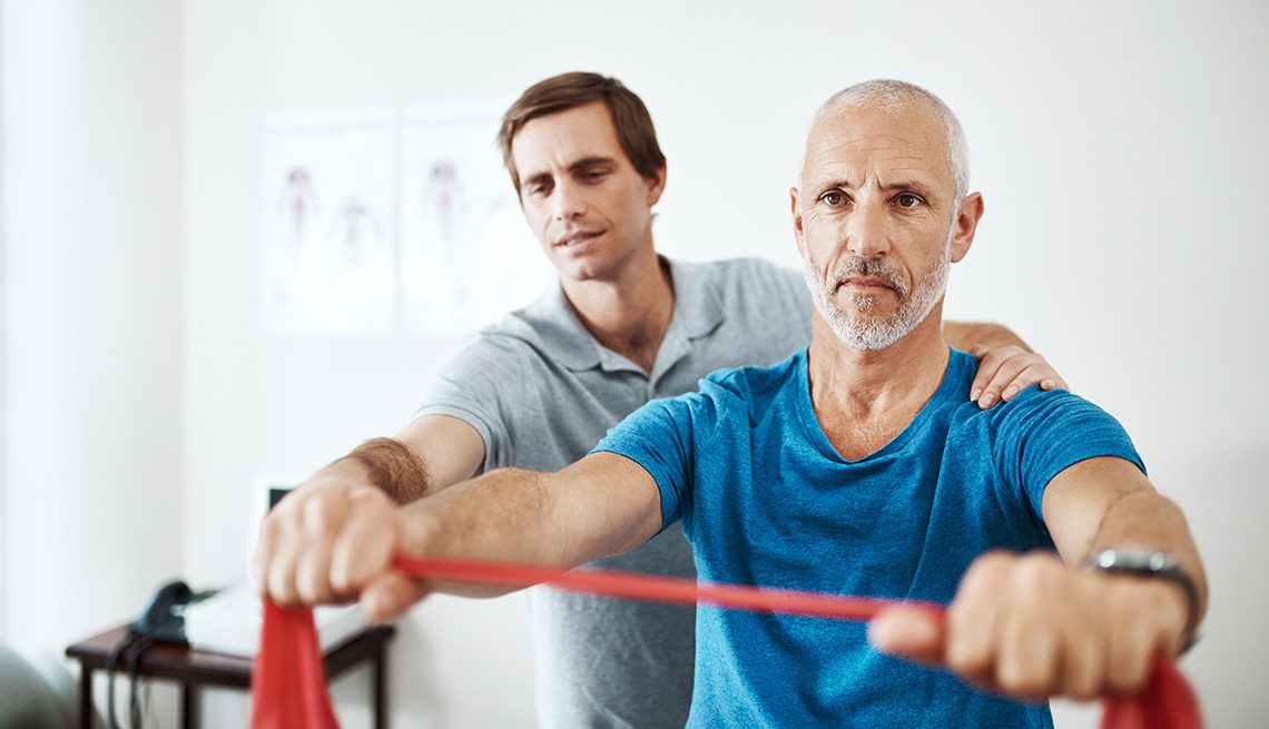 Physical therapist guiding senior male patient through resistance band exercise during rehabilitation.