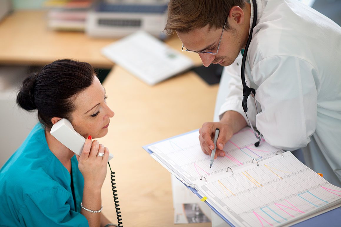 teamwork: young male doctor is looking into an organizer while his female assistant is listening at the phone