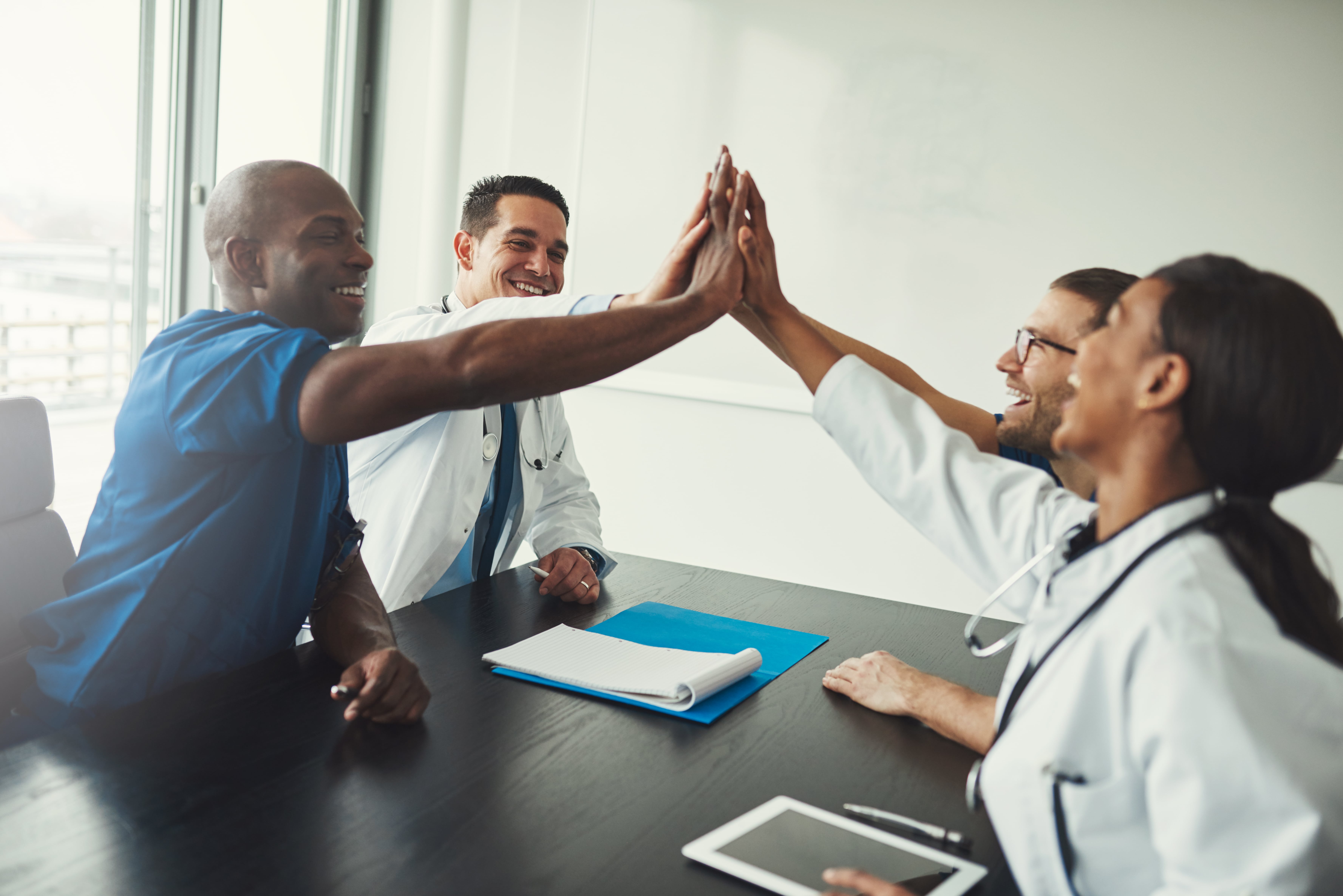 Physicians sitting at desk smiling and high-fiving each other