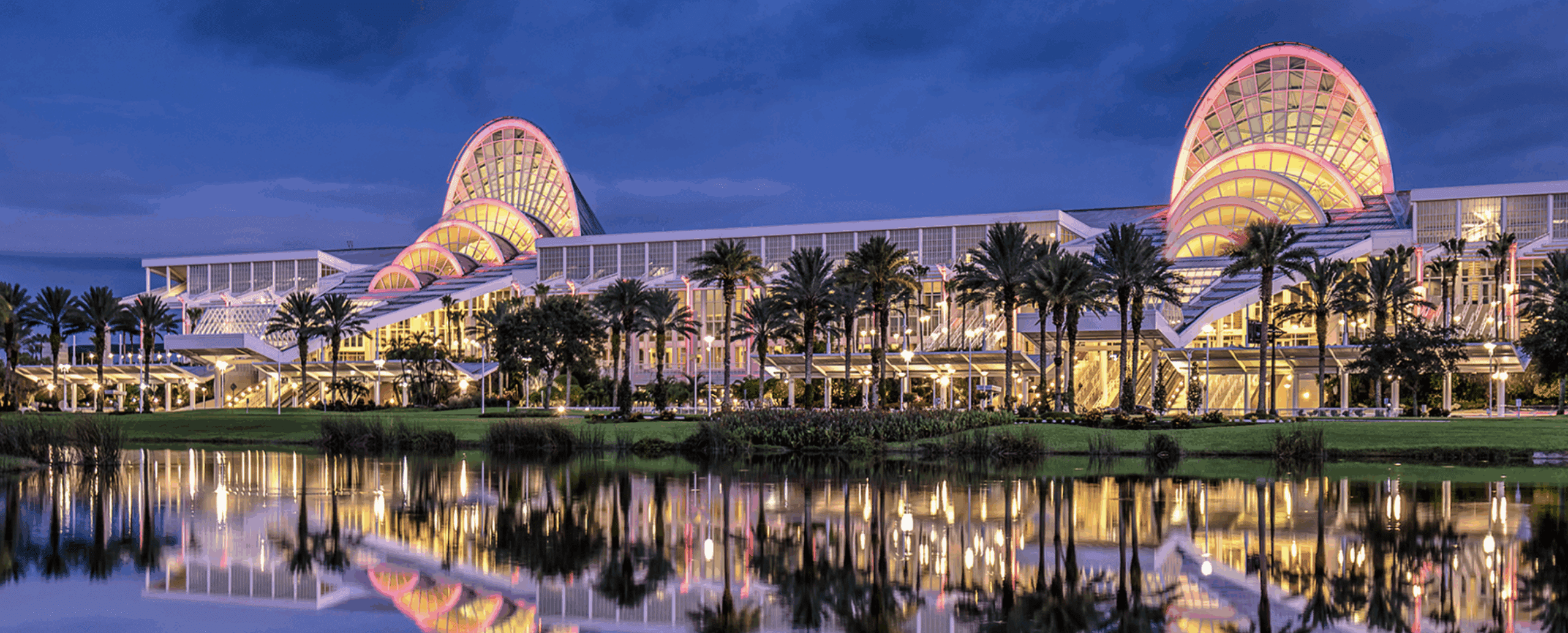 Exterior view of the ASHA 2019 Convention center illuminated at night with palm trees and reflections.